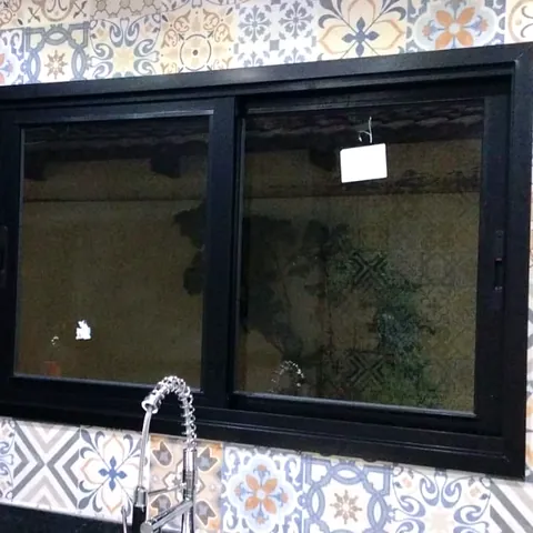 Janela de correr de duas folhas em alumínio preto, instalada pela CCS Vidros acima da bancada de uma cozinha.
